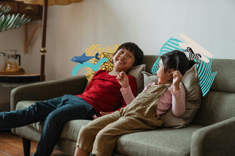 Brother and sister sitting on the couch happy and laughing with the representation of their Totem emerging from behind them. 